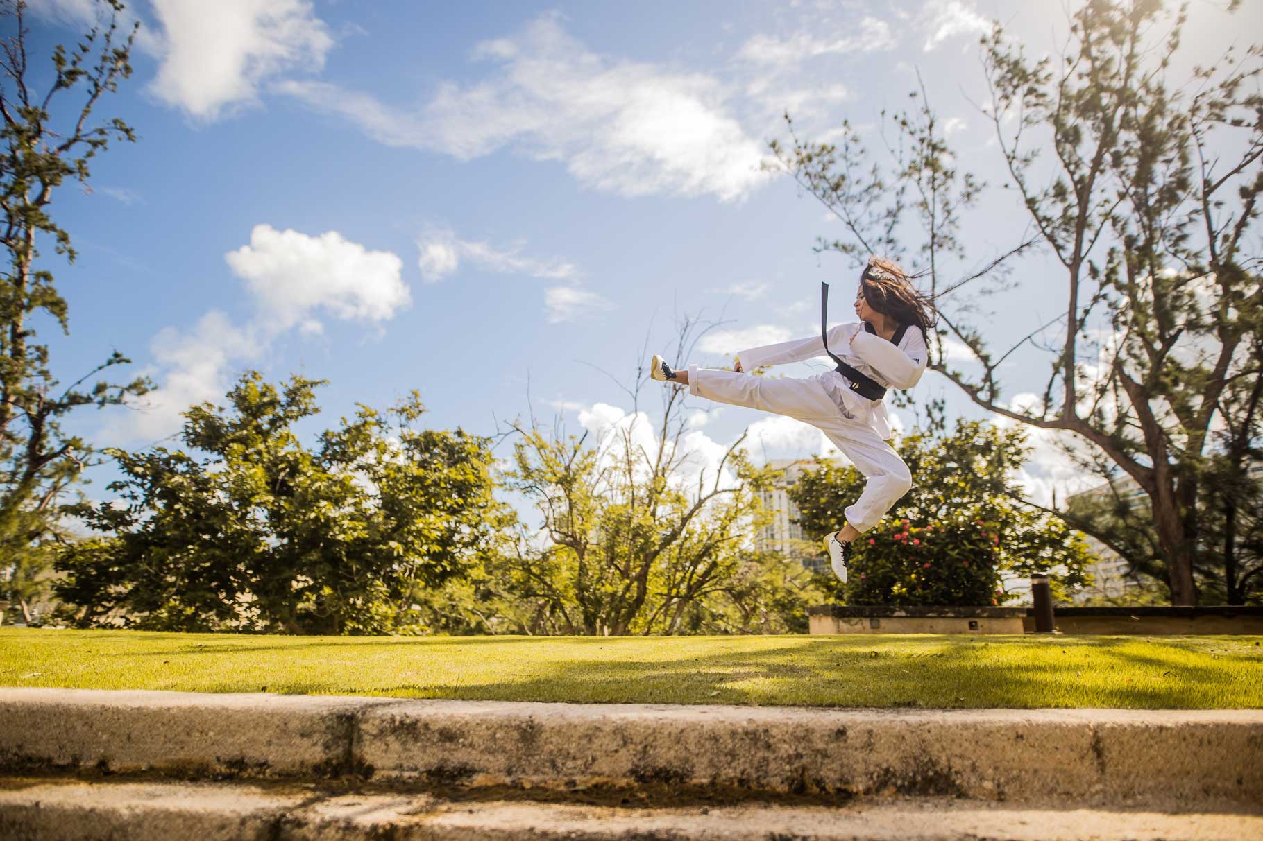 mujer cinturón negro realizando un salto de kata en un entorno verde bajo un cielo azul